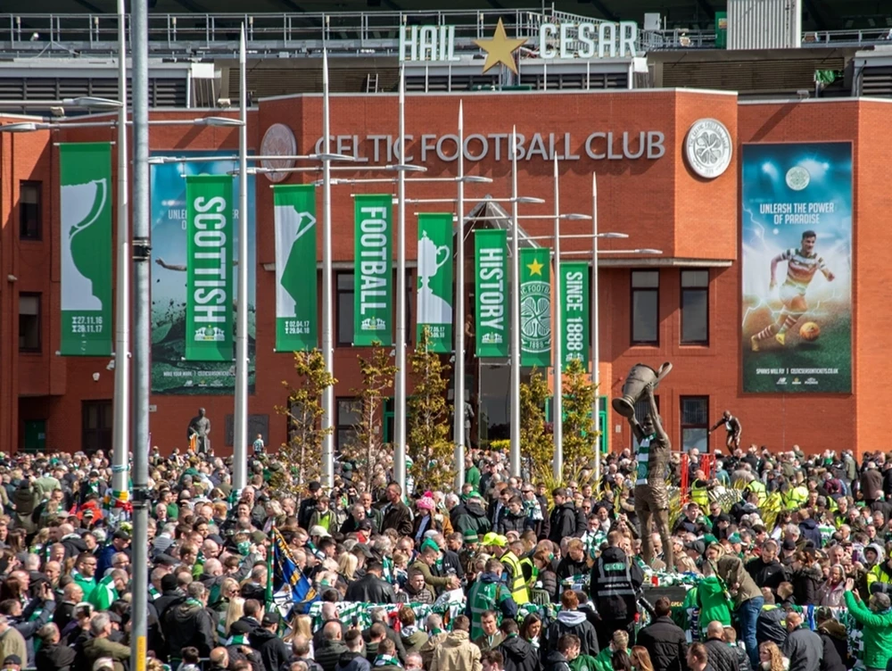 Eine riesige Menschenmenge von Fußballfans versammelt sich am Spieltag vor der Backsteinfassade und den grünen Bannern des traditionsreichen Stadions in Glasgow.